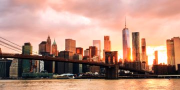 New York, USA. View of Manhattan bridge and Manhattan in New York, USA at sunset. Colorful cloudy sky with skyscrapers. Sun setting behind the skyscrapers