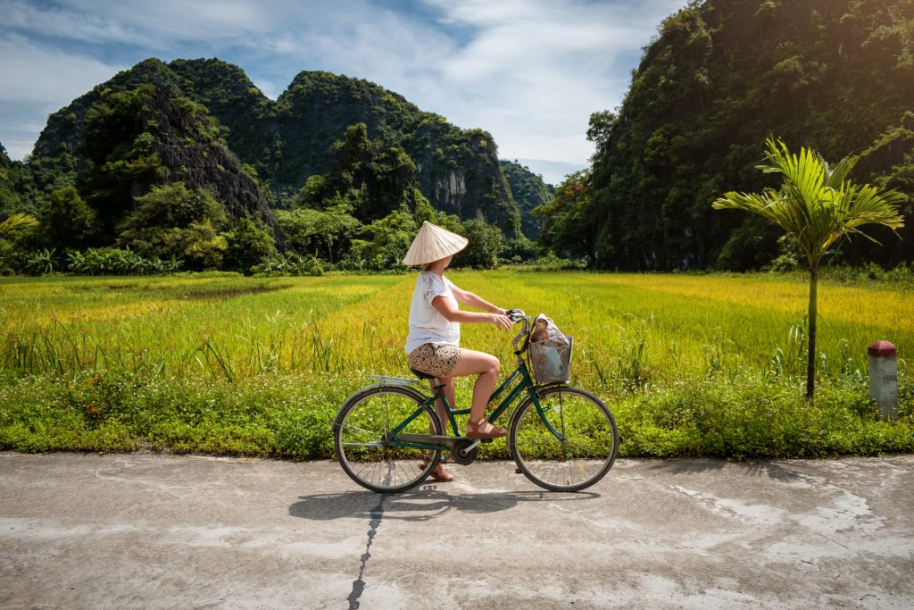 Woman,Tourist,Riding,A,Bicycle,Through,Rice,Fields,In,Vietnam.